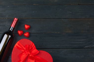 Sevgililer Günü tebrik kartı. Kırmızı gül çiçekleri, şarap ve hediye kutusu ahşap masada..