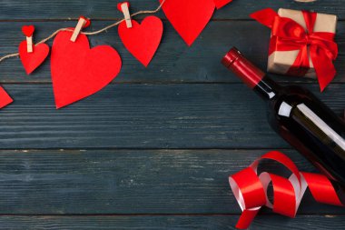 Sevgililer Günü tebrik kartı. Kırmızı gül çiçekleri, şarap ve hediye kutusu ahşap masada..