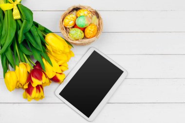 mesaj için tablet ekranı ve renkli laleler ve ahşap zemin üzerinde paskalya yumurtaları