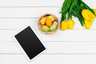mesaj için tablet ekranı ve renkli laleler ve ahşap zemin üzerinde paskalya yumurtaları