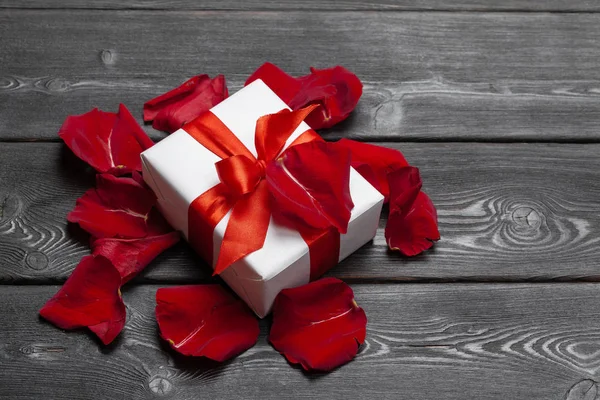 Ahşap arka plan üzerinde hediye kutusu ve gül yaprağı.