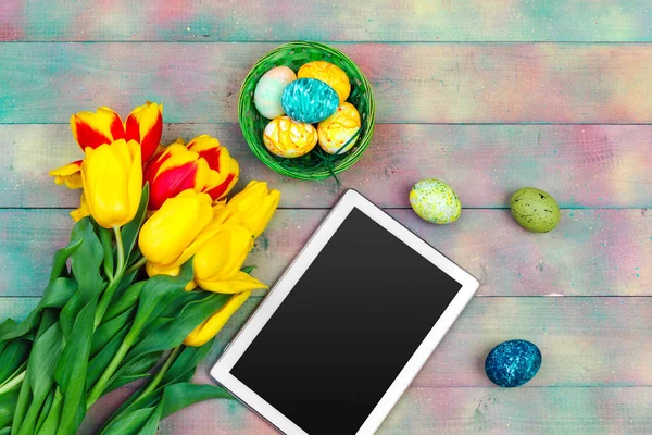 mesaj için tablet ekranı ve renkli laleler ve ahşap zemin üzerinde paskalya yumurtaları