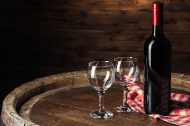 Şişe ve bir kadeh kırmızı şarap. Tahta fıçı üzerinde. Koyu ahşap arka planda.