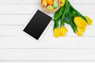 mesaj için tablet ekranı ve renkli laleler ve ahşap zemin üzerinde paskalya yumurtaları