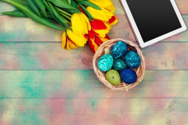 mesaj için tablet ekranı ve renkli laleler ve ahşap zemin üzerinde paskalya yumurtaları
