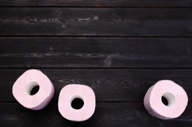 Pastel pembe tuvalet kağıdı siyah ahşap arka planda yuvarlanıyor.