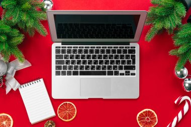 Kırmızı arka plan üst görünümünde kürk ağacı dalları ve noel süslemeleri ile Laptop