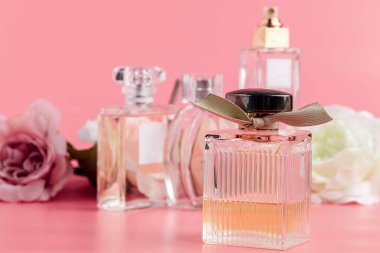 Pembe kumaş arka planında güller olan parfüm şişesi. 