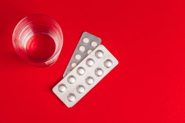 Kabarcıklardaki haplar ve kırmızı arka plan manzaralı bir bardak su. İlaç.