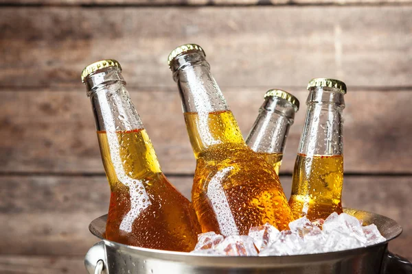 Cold bottles of beer in the bucket on the wooden background