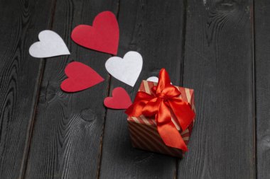 Sevgililer Günü için kırmızı kurdeleli hediye kutusu ve tahta arka planda kağıt kalpler.