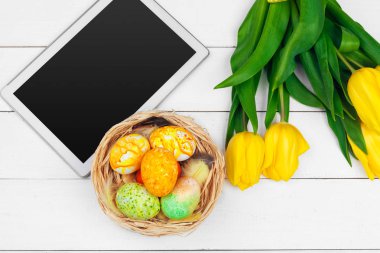 mesaj için tablet ekranı ve renkli laleler ve ahşap zemin üzerinde paskalya yumurtaları