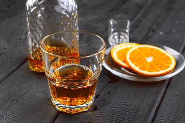 Koyu ahşap arka planda portakal meyveli viski bardağı.