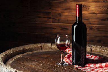 Şişe ve bir kadeh kırmızı şarap. Tahta fıçı üzerinde. Koyu ahşap arka planda.