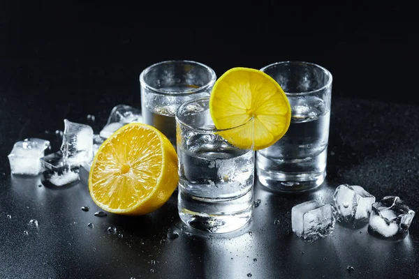 Cold vodka in shot glasses on a black background.