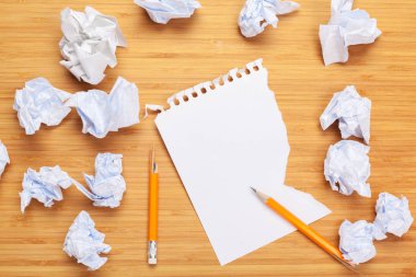 Tahta bir masanın üzerindeki beyaz not defteri. Defterlerin etrafında bir sürü buruşuk kağıt var.