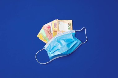 Tıbbi yüz maskesi ve mavi arka planda Ukrayna Hryvnia banknotları