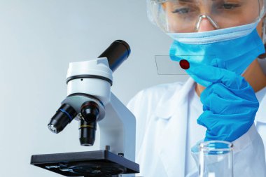 Laboratuvarda mikroskop yakınında kan örneği olan bir kadın bilim adamı incelemesi yapıyor.