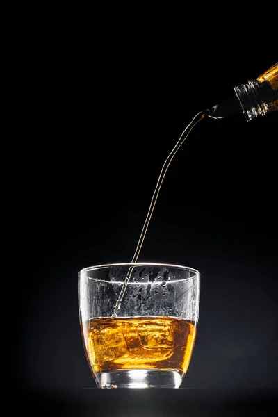 Whisky derramando em um copo no fundo preto — Fotografia de Stock