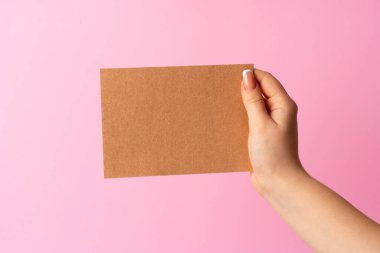 Pembe arka planda boş kartvizit gösteren kadın eli.