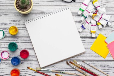 Çizim aletleri, sabit malzemeler, sanatçının çalışma yeri. Suluboya resimler ve ahşap masadaki boş not defteri.