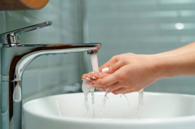 Ellerini banyo lavabosunda yıkayan bir kadının yakın çekimi.