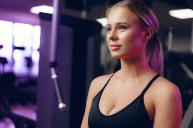 Spor sutyenli, koyu renk bir spor salonunda genç sarışın bir kadının portresi.