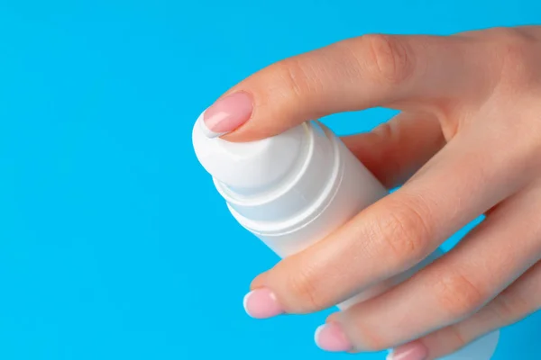 Vrouwelijke hand houden huidverzorgingsproduct fles op blauw — Stockfoto