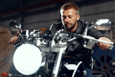 Motosikletli bir adam yeraltı otoparkında motosikletinin üstünde oturuyor.