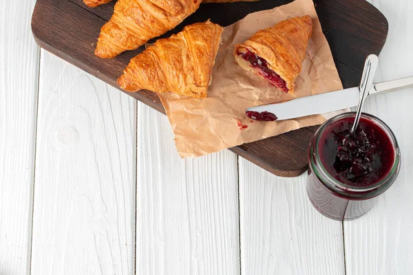 Fresh croissants with berry jam on dark wooden board — Stock Photo, Image