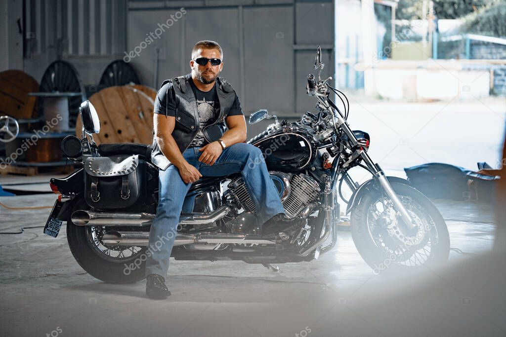 Bearded motorcyclist in black leather clothing with his motorbike