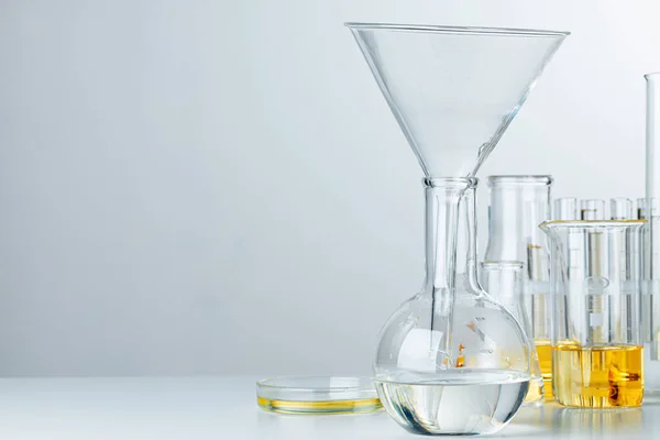 Laboratory glassware with yellow oily liquid on grey background — Stock Photo, Image