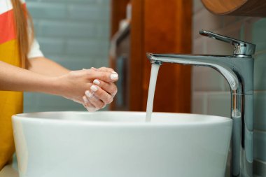 Ellerini banyo lavabosunda yıkayan bir kadının yakın çekimi.