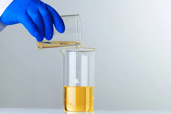 과학자나 파란 장갑을 낀 의사가 플라스크에 노란 액체를 부어 넣는 모습 — 스톡 사진