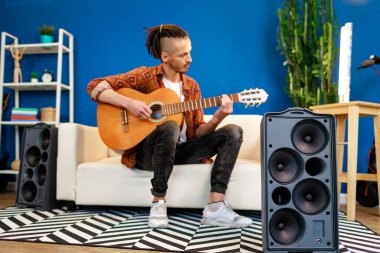 Kafkasyalı genç bir adam kanepeye oturmuş akustik gitar çalıyor.