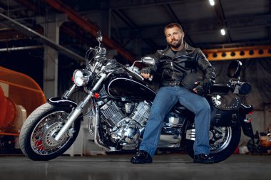 Siyah deri elbiseli motosikletli sakallı bir motosikletli.
