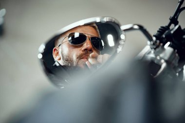 Motosiklet aynasında güneş gözlüklü bir adamın yansıması.