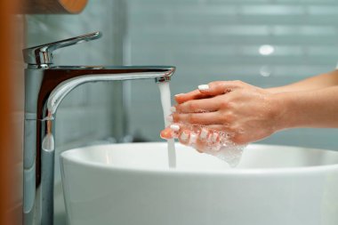 Ellerini banyo lavabosunda yıkayan bir kadının yakın çekimi.