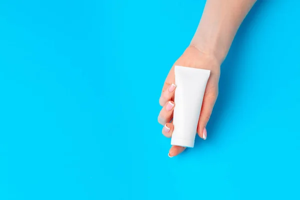 Mão feminina segurando garrafa de produto skincare em azul — Fotografia de Stock