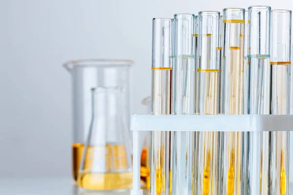 Wyroby laboratoryjne ze szkła z żółtym oleistym płynem na szarym tle — Zdjęcie stockowe