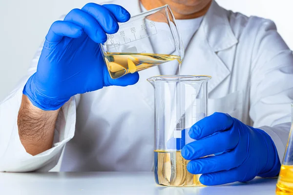身穿蓝色手套的科学家或医生把一些黄色液体倒入瓶中 — 图库照片