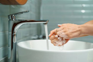 Ellerini banyo lavabosunda yıkayan bir kadının yakın çekimi.