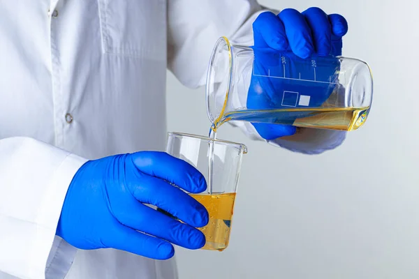 Ученый или доктор в синих перчатках наливает немного желтой жидкости во фляжку — стоковое фото