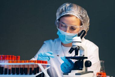 Laboratuvarda mikroskop yakınında kan örneği olan bir kadın bilim adamı incelemesi yapıyor.