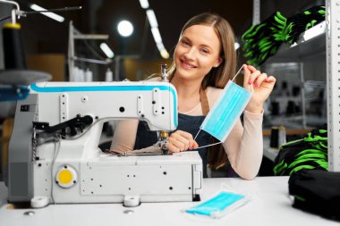 Gülümseyen genç sarışın terzi tıbbi koruyucu maske takıyor.