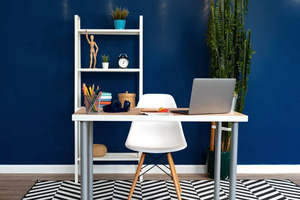 Mesa de trabajo con portátil contra pared azul en piso moderno —  Fotos de Stock