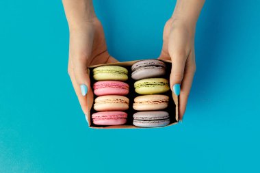 Kadınların elleri renkli badem kurabiyeleriyle dolu bir kutu tutuyor.