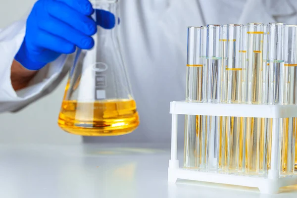 Wetenschapper of arts in blauwe handschoenen gieten wat gele vloeistof in een kolf — Stockfoto