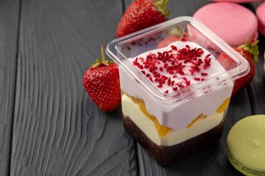 Siyah ahşap masada plastik şeffaf kutuda kremalı tatlı.