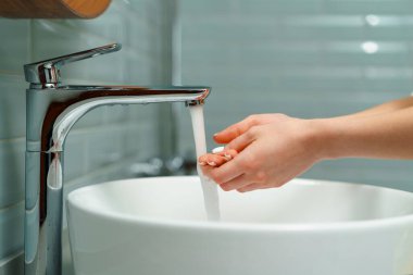Ellerini banyo lavabosunda yıkayan bir kadının yakın çekimi.